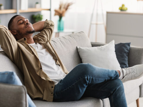 African American Guy Relaxing With Eyes Closed Sitting On Sofa Indoors